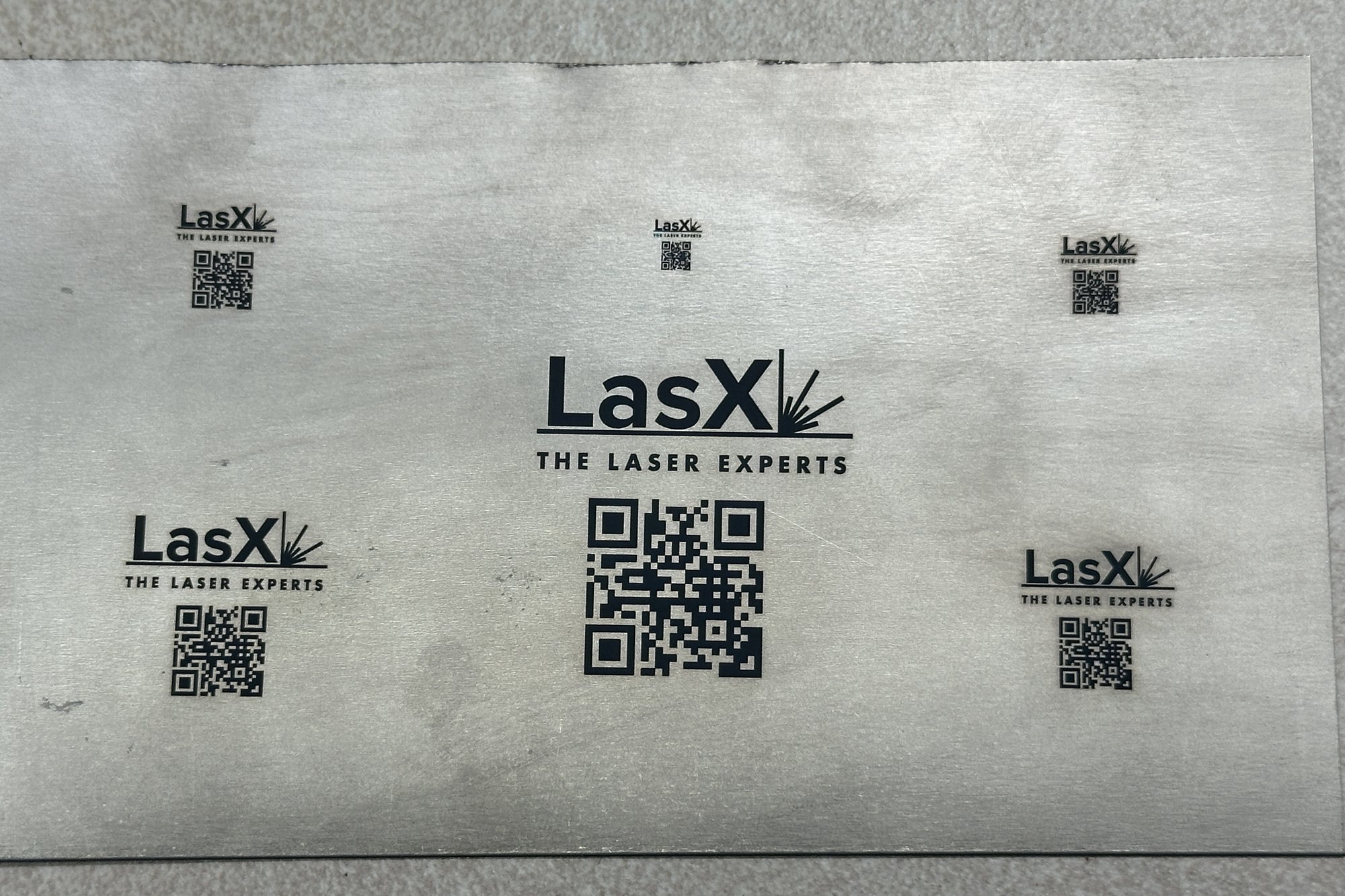 LasX logos and QR codes laser-marked in black on a titanium sheet