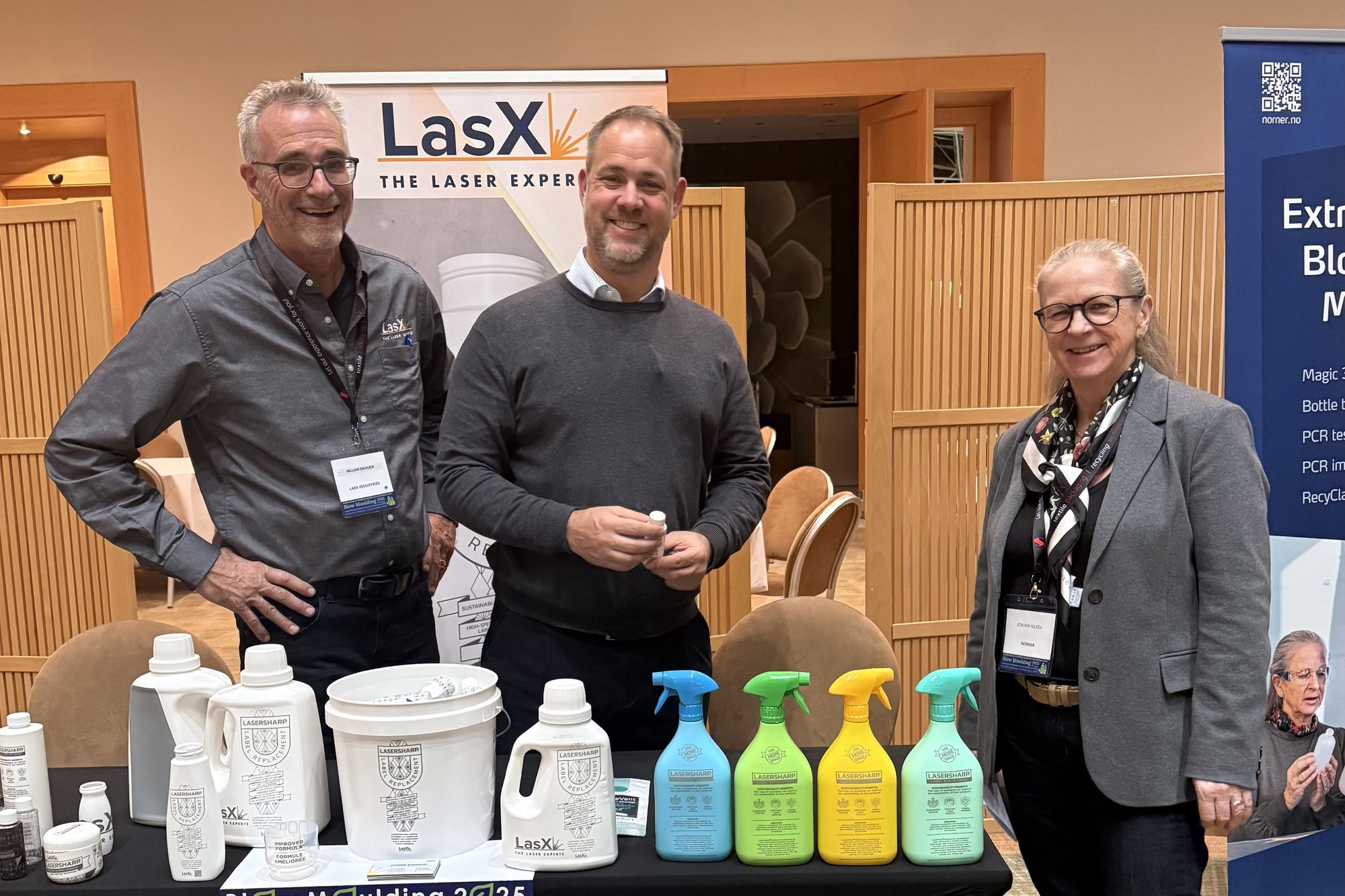 Three LasX team members at the LasX stand with laser-marked bottles and spray containers