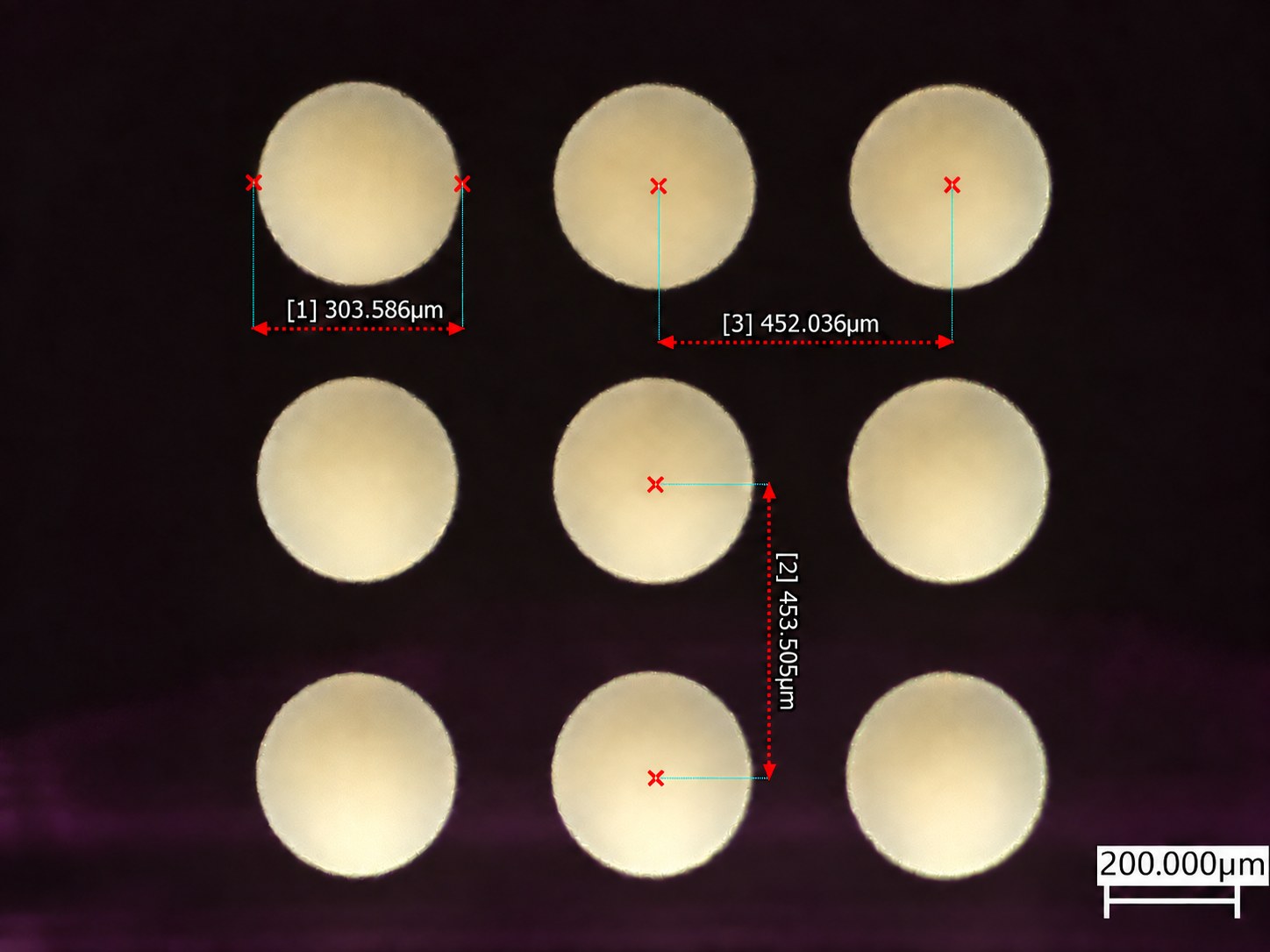 3 × 3 array of 300 µm laser-drilled through-glass vias on a 450 µm pitch, transmitted-light micrograph with measurements