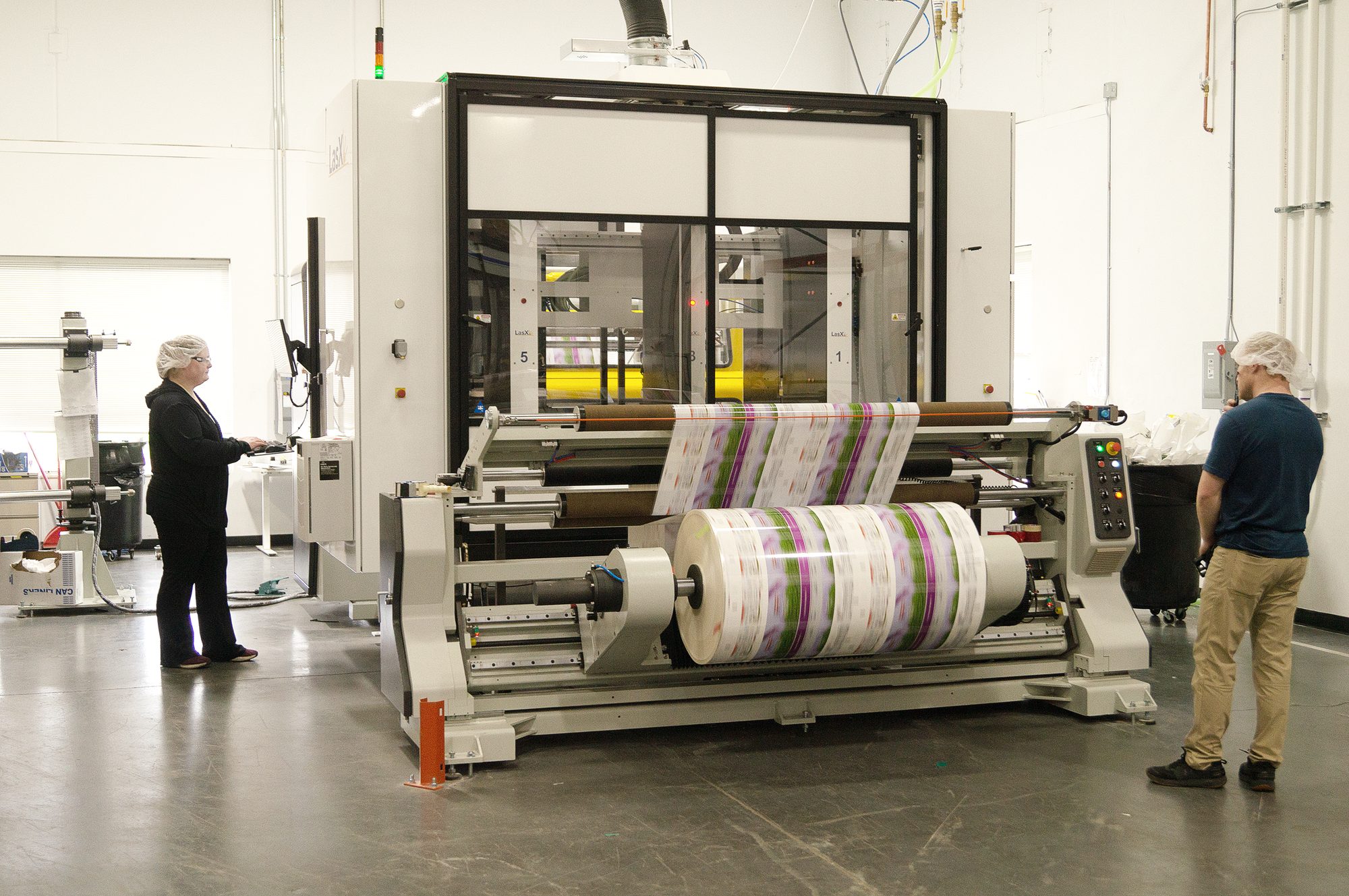 Two operators at a FocusPro line mounted over a slitter-rewinder, printed flexible packaging web running