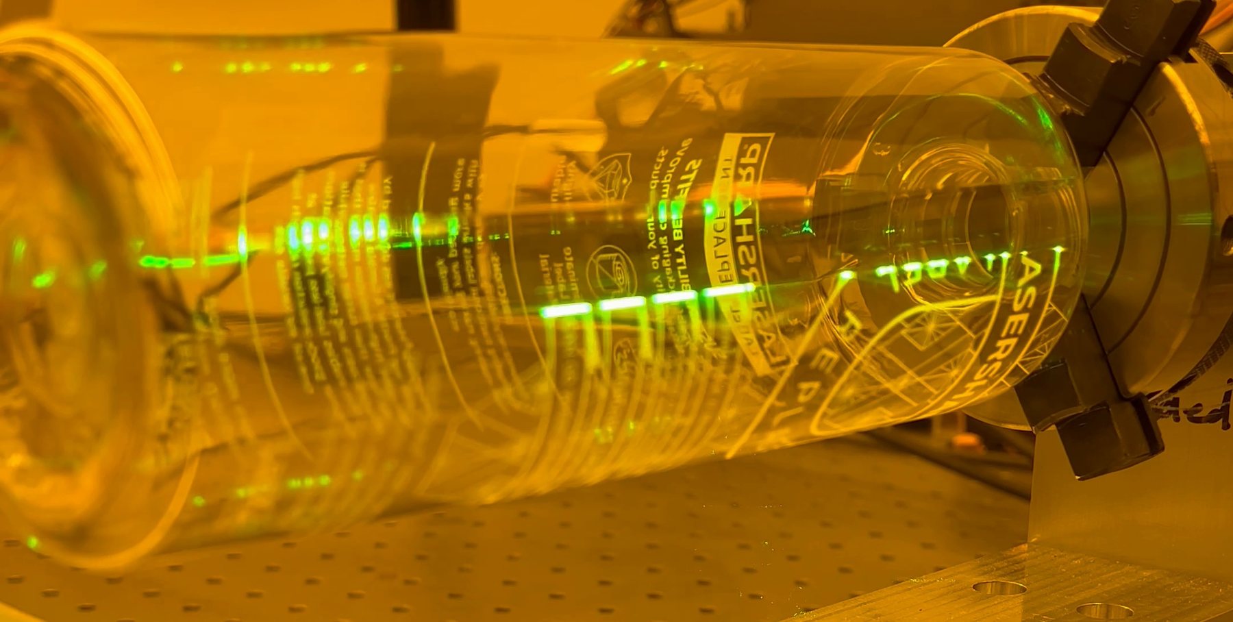 Clear bottle held in a rotation fixture being marked with a green laser