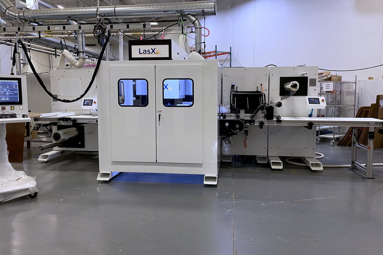 SmartFinish™ roll-fed laser finishing machine on the LasX floor — unwind, enclosed laser cell, and part take-off conveyor